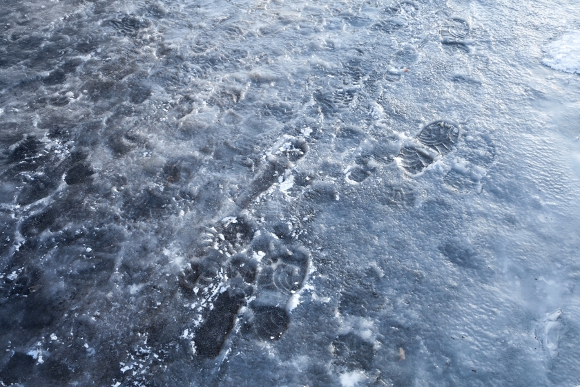 Pedestrians footprints in road blue ice. Street sleet background